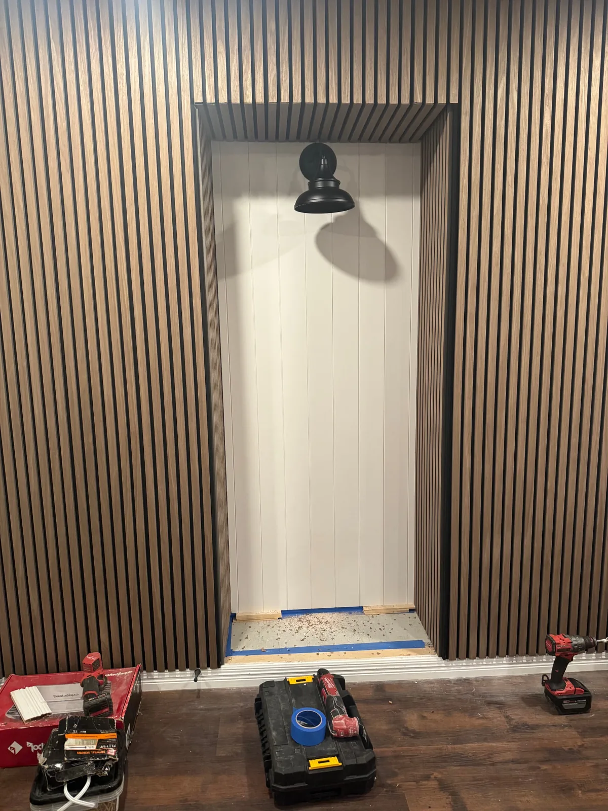 Completed entryway niche framed with warm wood-slat panels and a black wall light.
