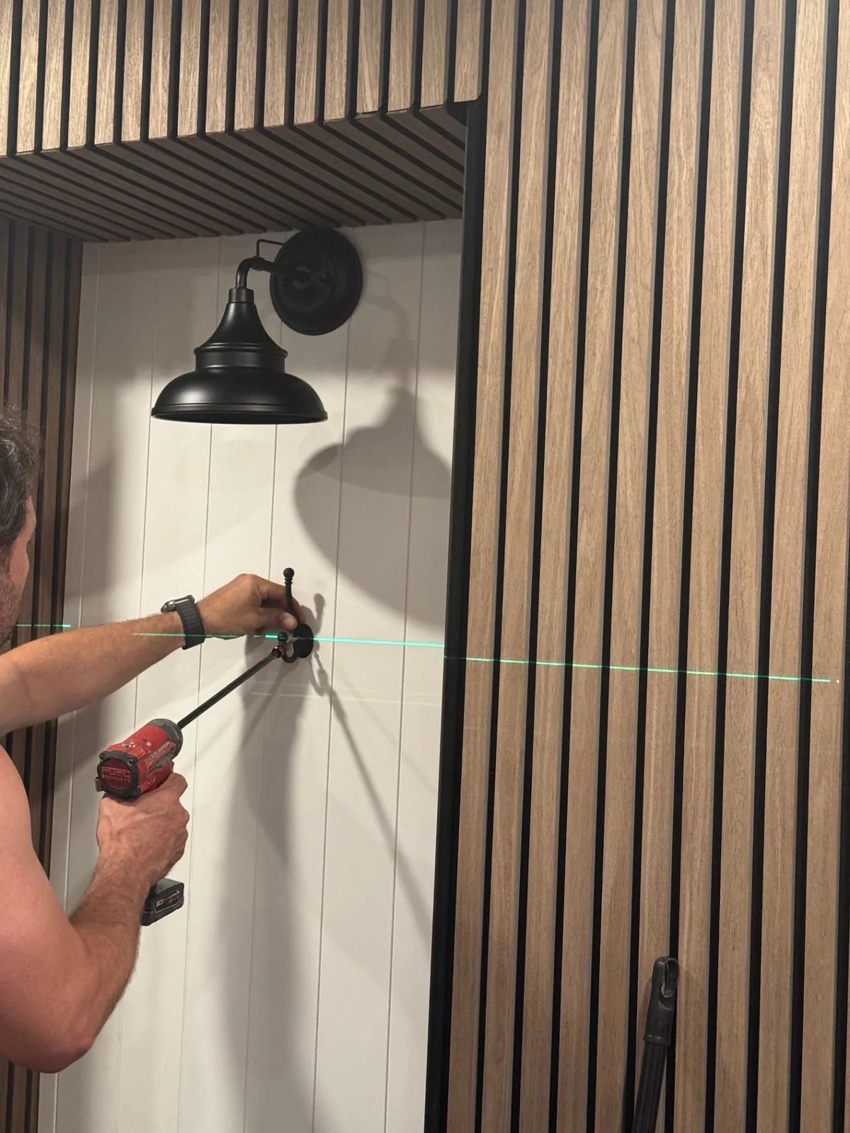 Close-up of the entryway wood-slat panels and black wall light during finish installation.